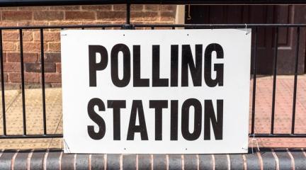 A sign reading "polling station" attached to railings outside the entrance to a building
