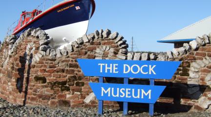 A curved stone wall. A boat. A sign that says The Dock Museum.