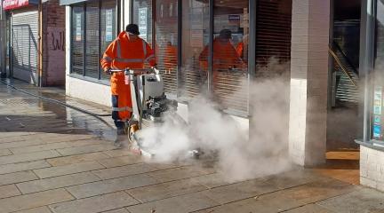 A man using a chewing gum removal machine on a pavement.