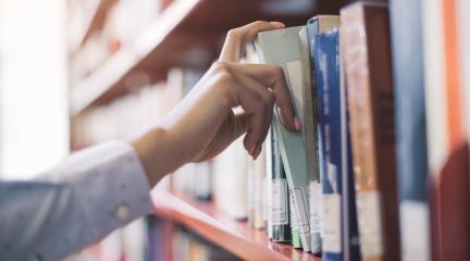 Person pulling a book off a library shelf