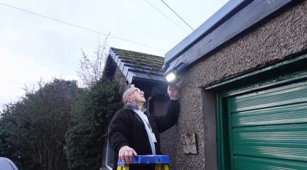 A man on a ladder fixing a light outside a garage.