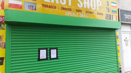 A closed shop with a green shutter. Sign reads: Easy Shop.