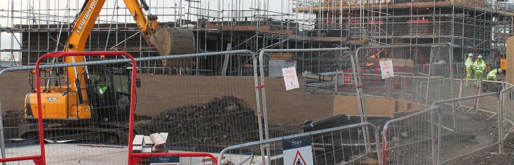 A building site with two house being built in the background and a digger in the foreground