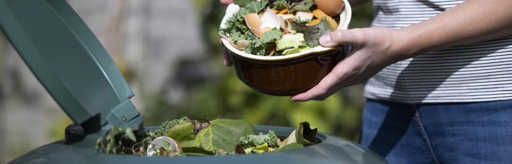 A person putting vegetable cuttings into a compost bin.