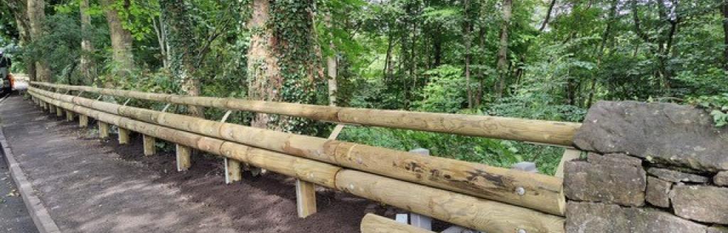 Wooden clad crash barriers on the side of a road with a forest as the backdrop