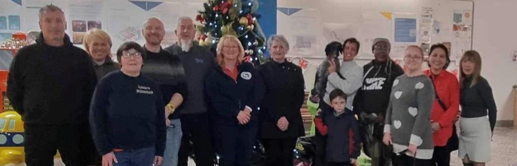 Men and women standing in front of a Christmas tree in Barrow Market.