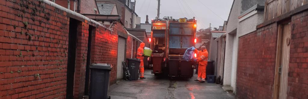 Two crew members in orange overalls loading recycling into the back of a wagon.