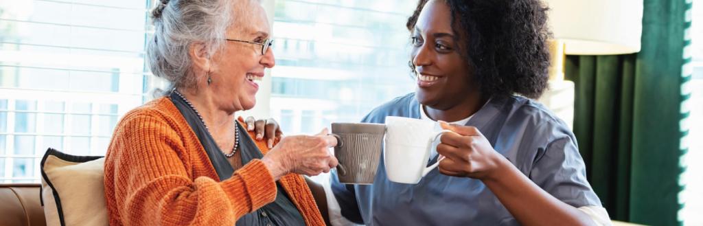 Two women sitting side by side holding mugs and chatting.