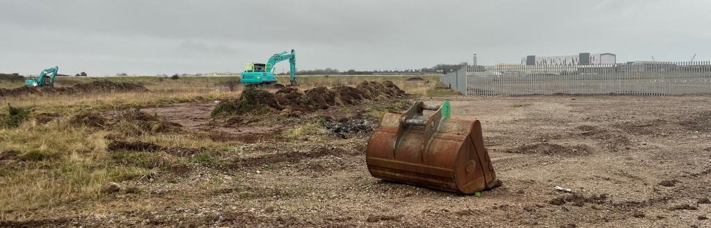 A digger in front of a cleared section of land.