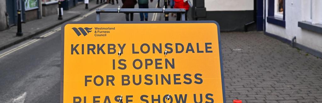 An orange road sign saying "Kirkby Lonsdale is open for business."