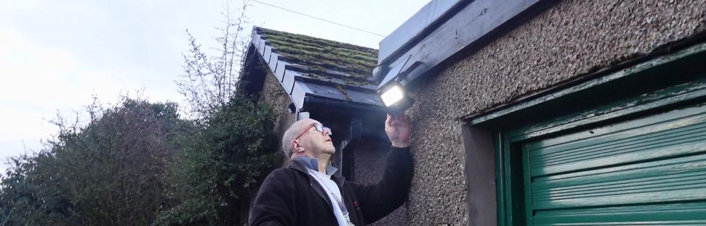 A man on a ladder fixing a light outside a garage.